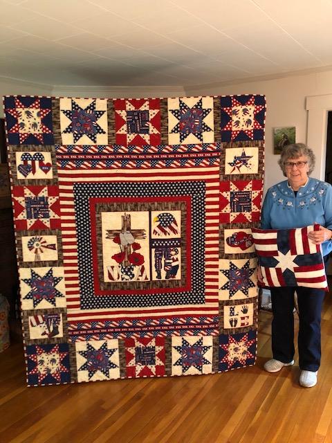 Maureen stands next to a large red, white, and blue quilt. 